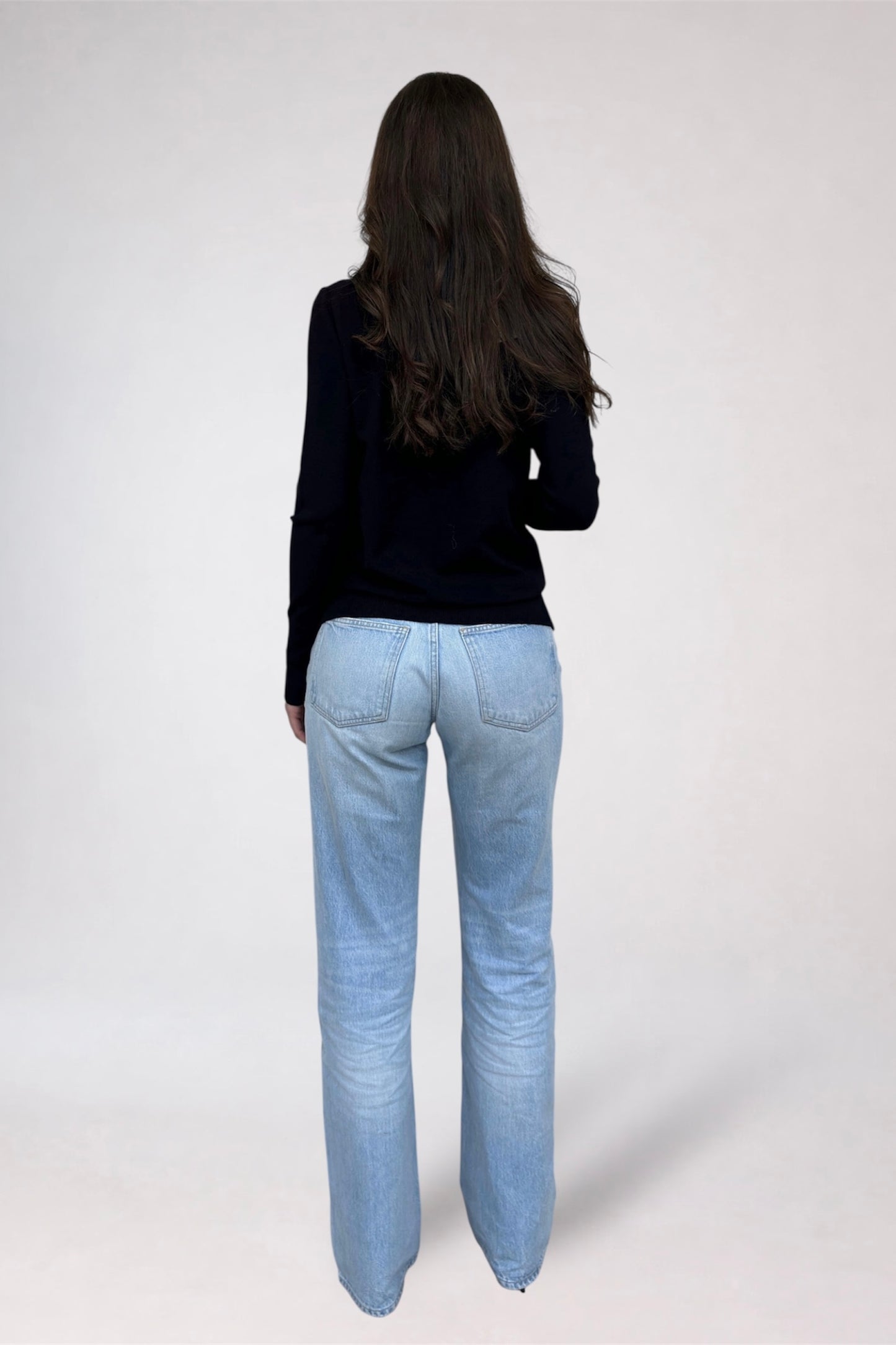 Person wearing light blue jeans and a black top on a white background