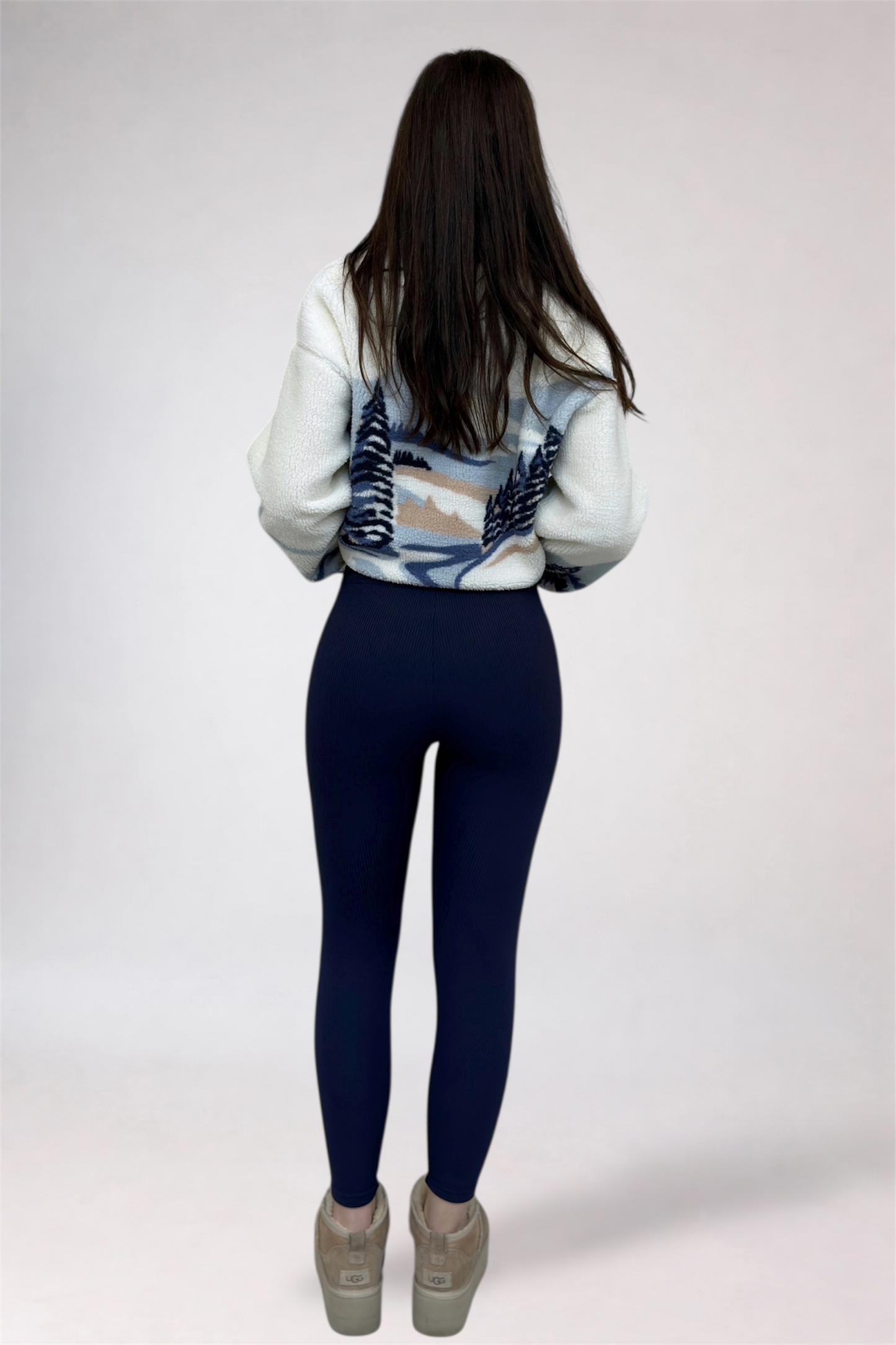 Person wearing a patterned sweater and dark blue leggings on a white background