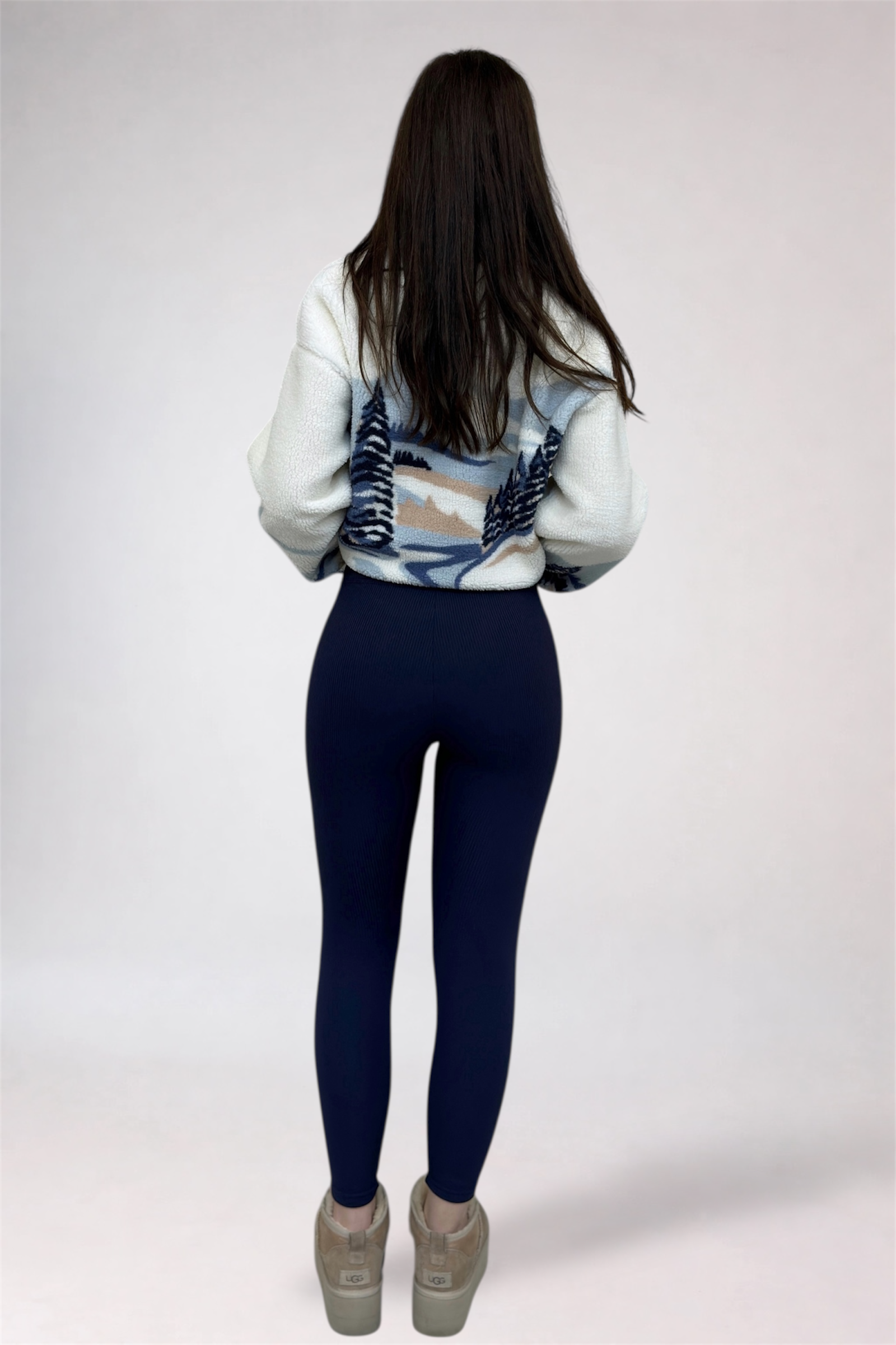 Person wearing a patterned sweater and dark blue leggings on a white background