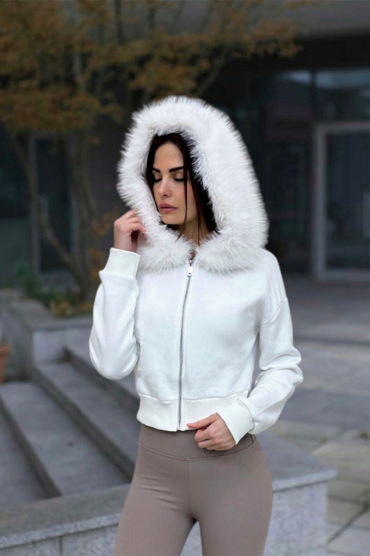 Woman wearing a white jacket with a fur-lined hood outdoors.