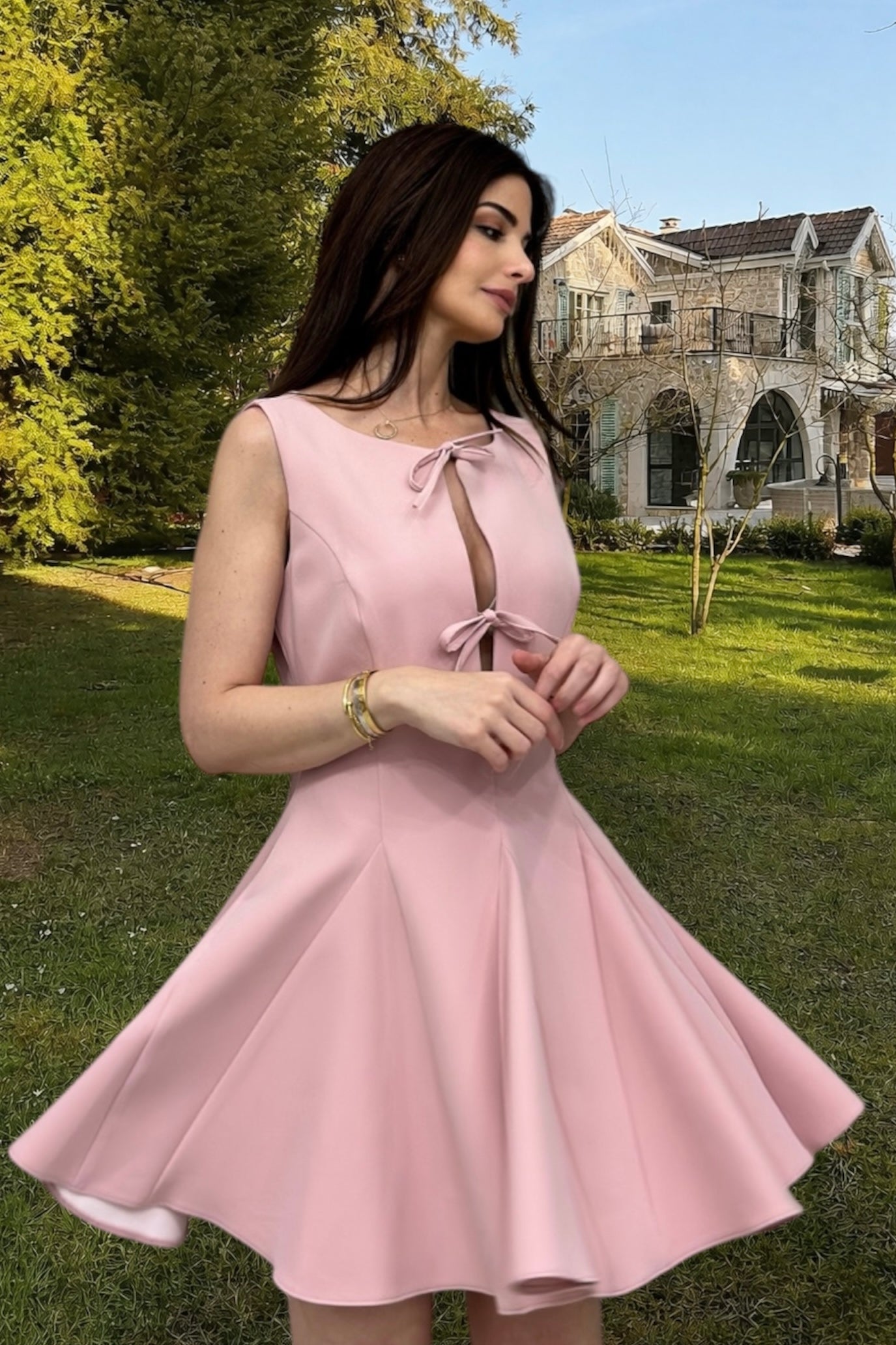 Woman in a pink dress standing outdoors with a house and trees in the background