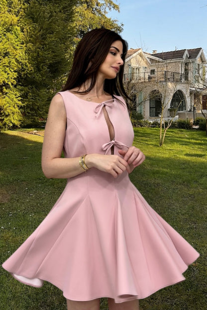 Woman in a pink dress standing outdoors with a house and trees in the background