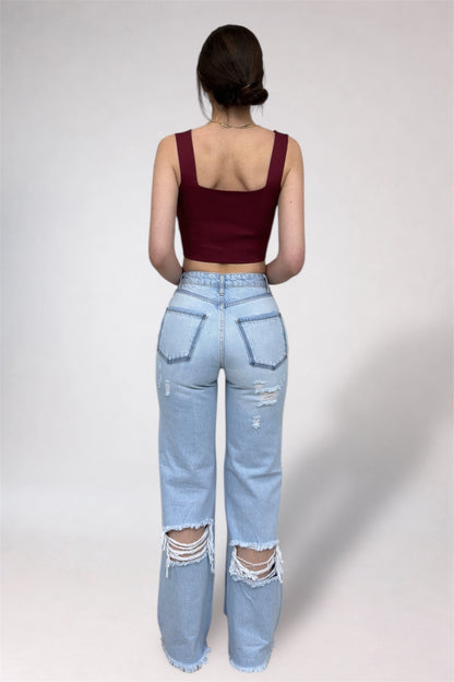 Person wearing a burgundy crop top and light blue ripped jeans on a plain background