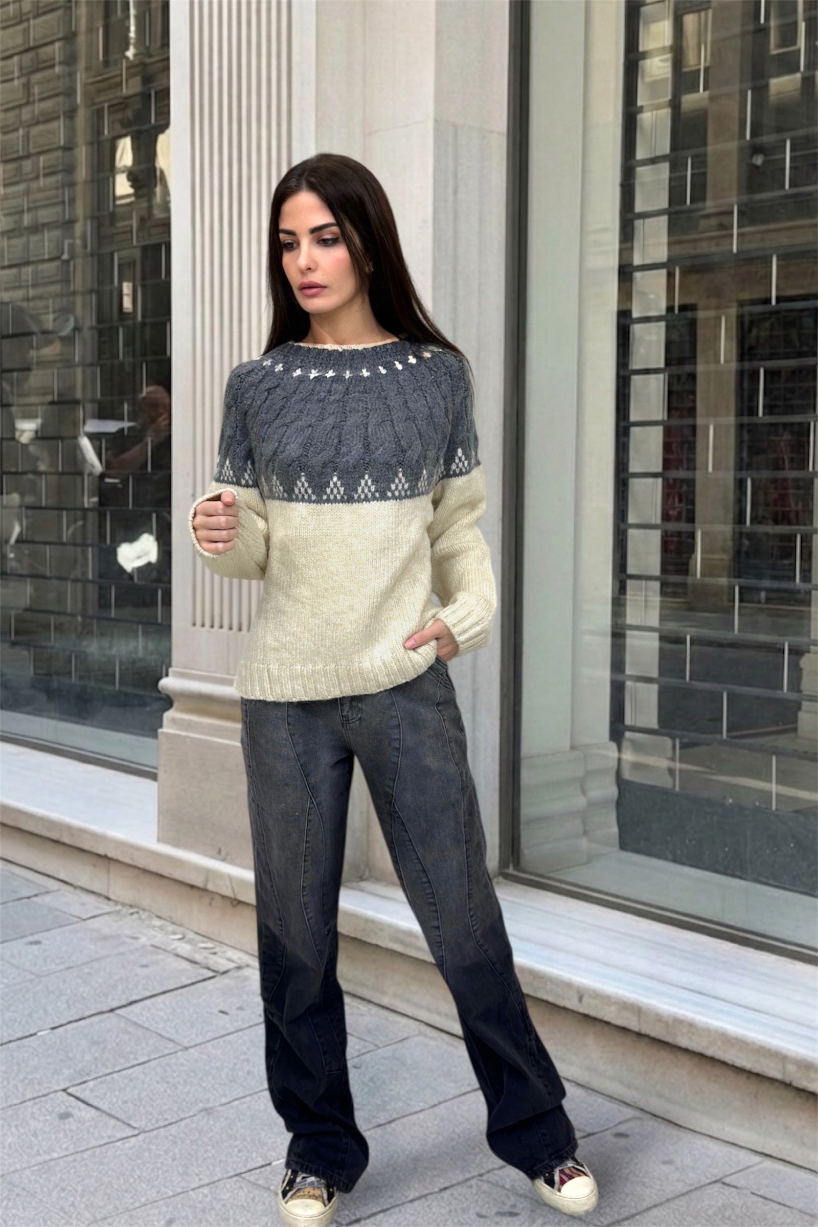 Woman wearing a two-tone sweater standing in front of a building with large windows.