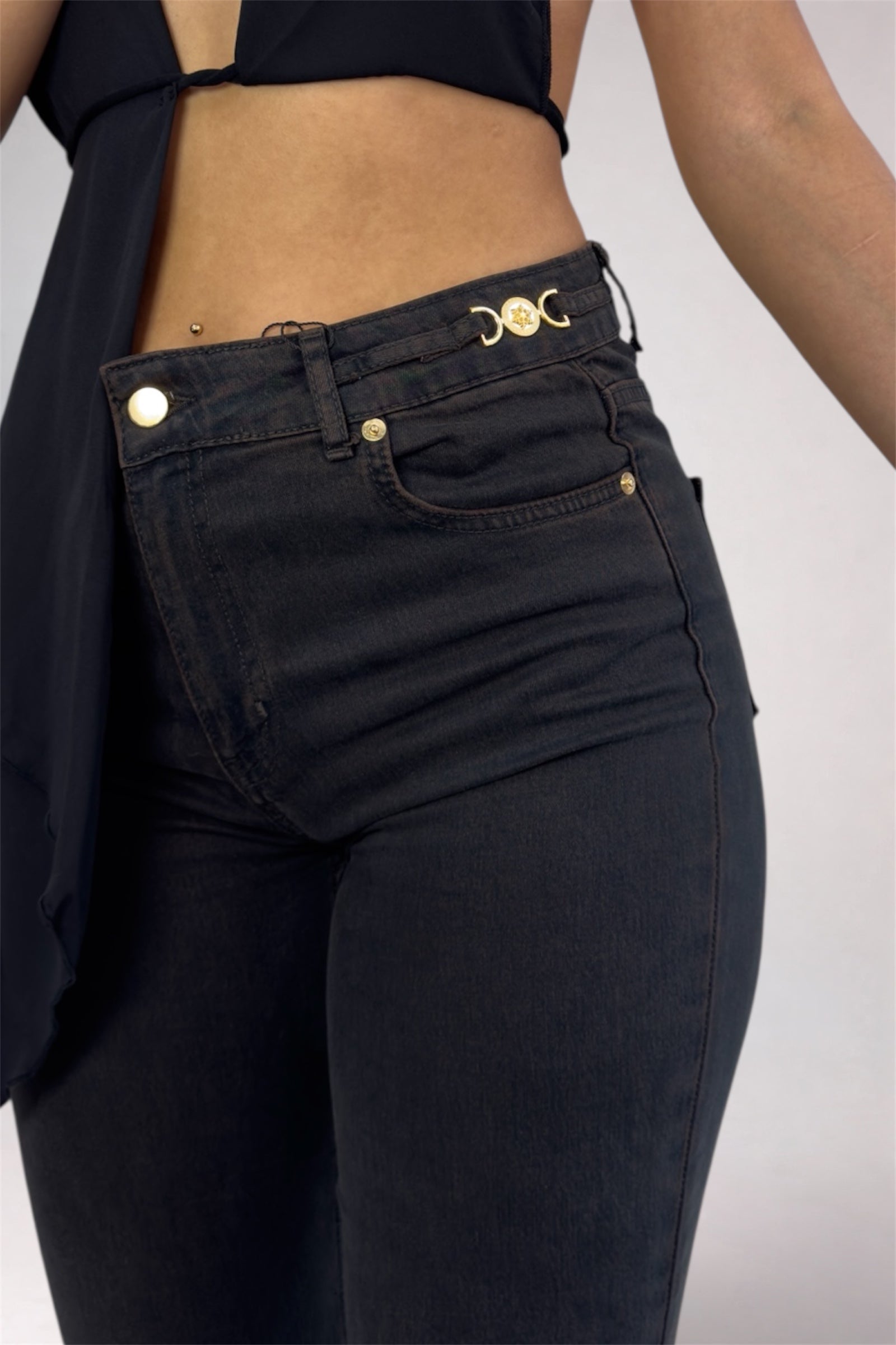 Person wearing black jeans with gold buttons on a plain background