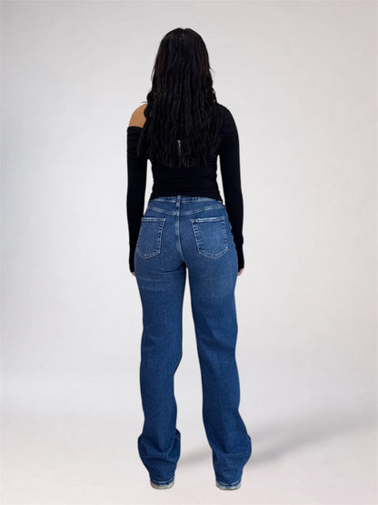 A woman viewed from the back wearing a black off-the-shoulder long-sleeve top and blue straight-leg jeans against a light gray studio background.