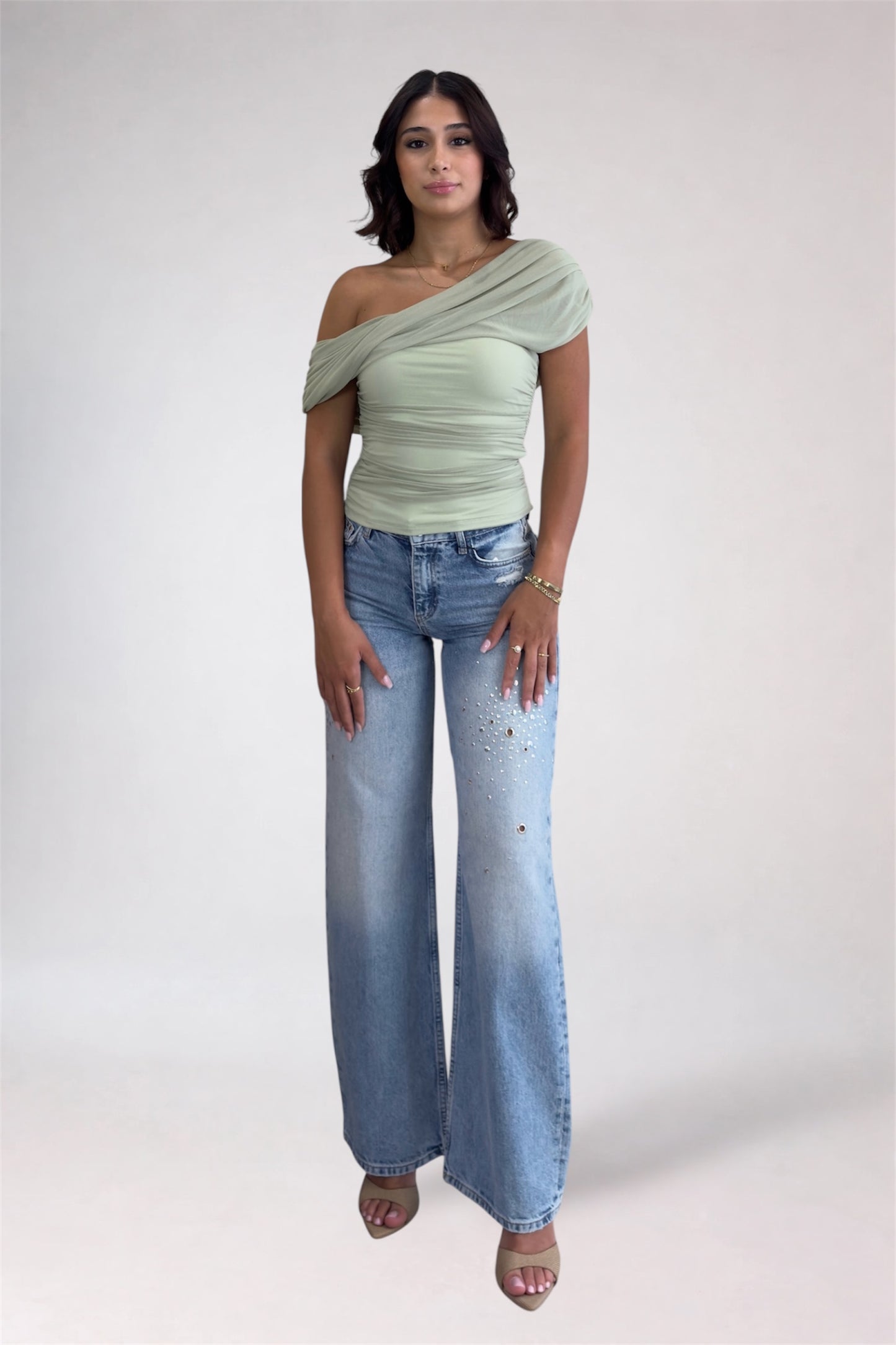 Woman wearing a light green off-shoulder top and blue jeans on a white background