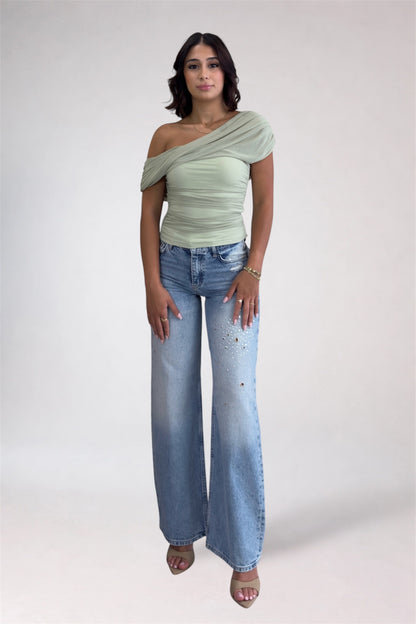 Woman wearing a light green off-shoulder top and blue jeans on a white background