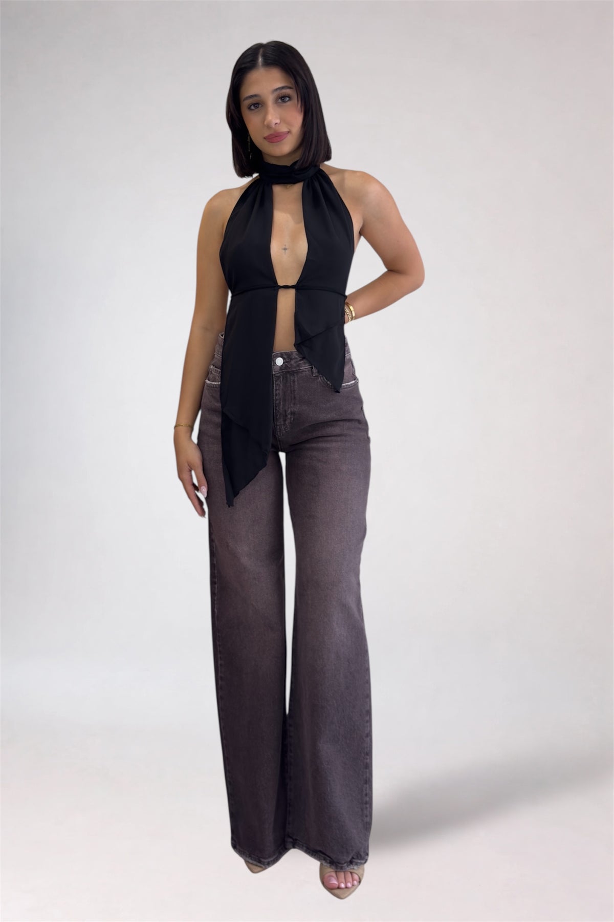 Woman wearing a black sleeveless top and wide-leg jeans on a white background