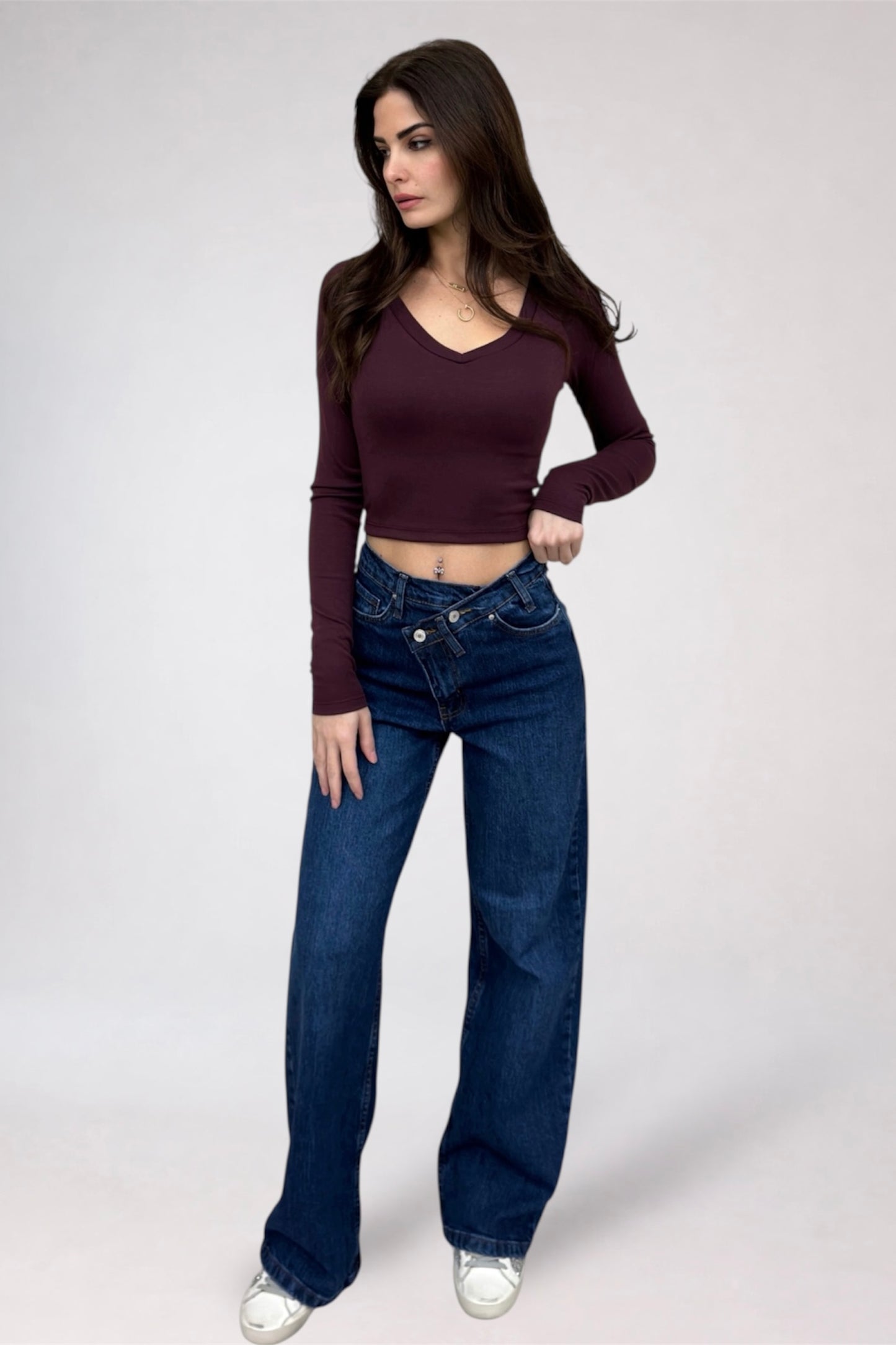 Woman wearing a maroon long-sleeve top and blue jeans on a white background