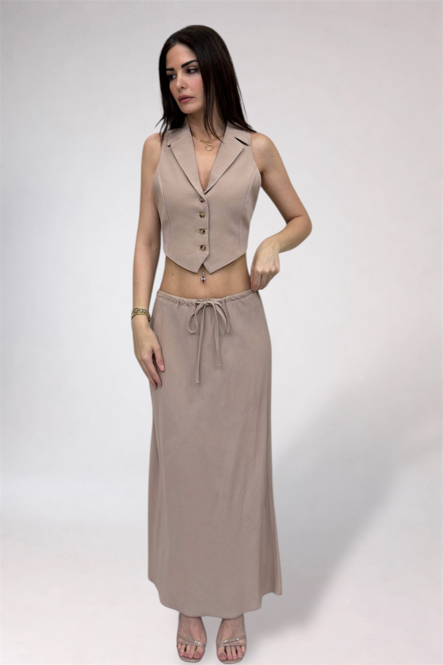 Woman wearing a beige vest and long skirt on a white background