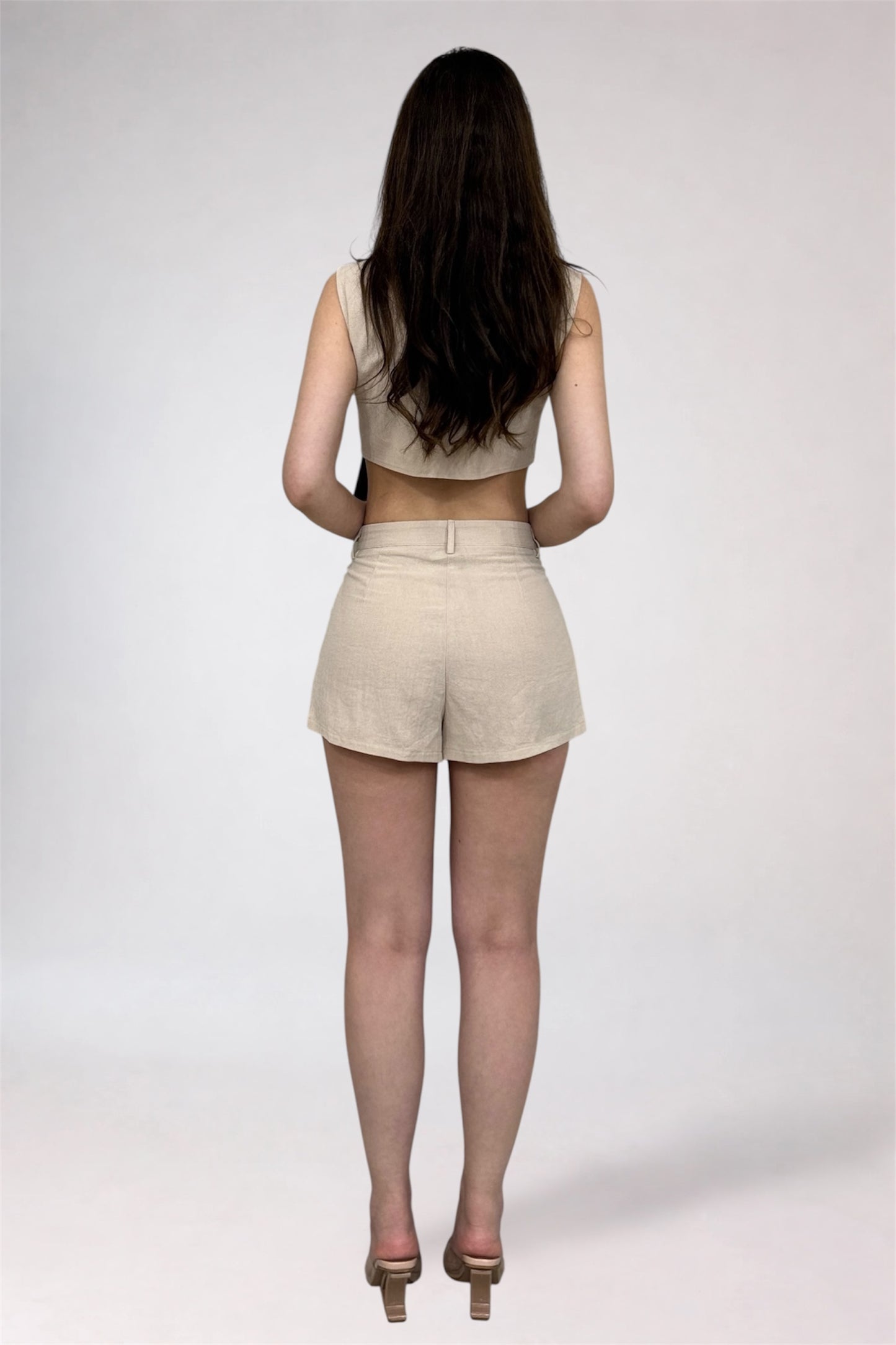 Woman wearing a beige sleeveless top and shorts on a white background