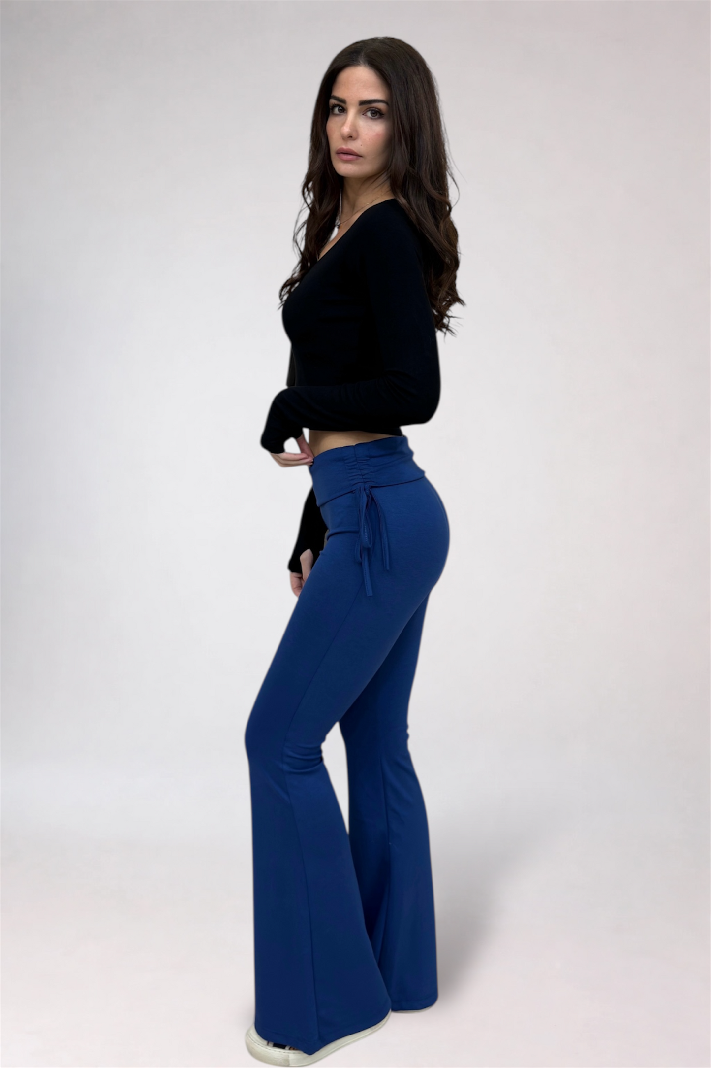 Woman wearing a black top and blue flared pants on a white background