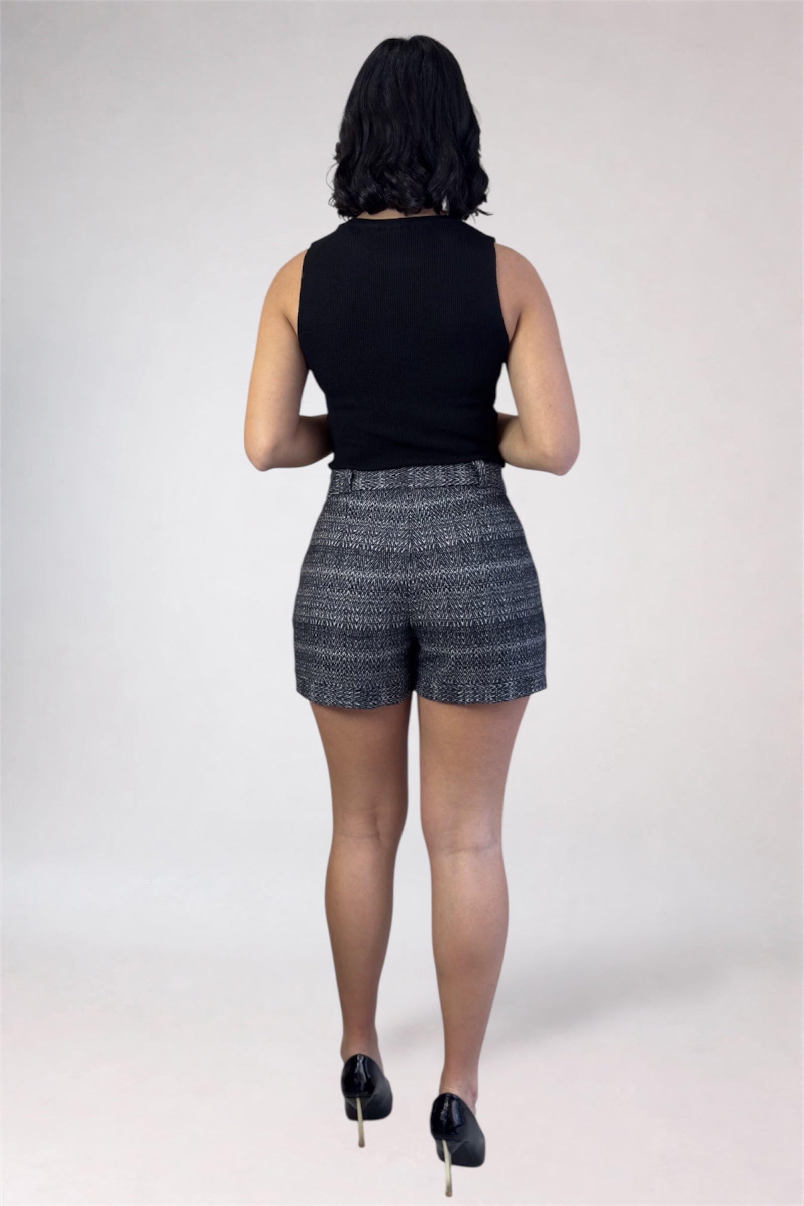 Person wearing a black sleeveless top and patterned shorts on a white background