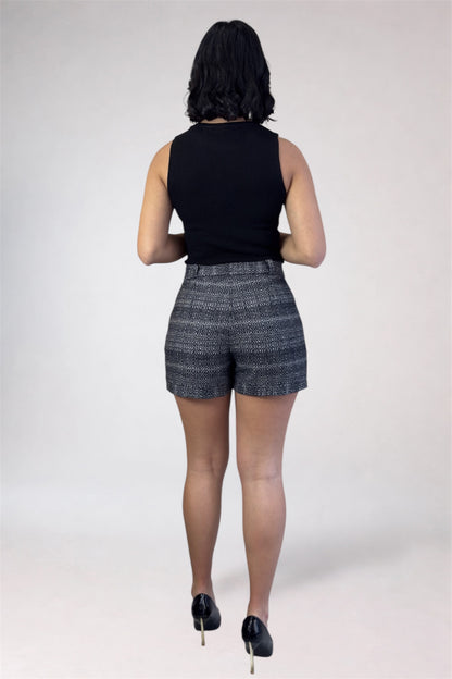 Person wearing a black sleeveless top and patterned shorts on a white background