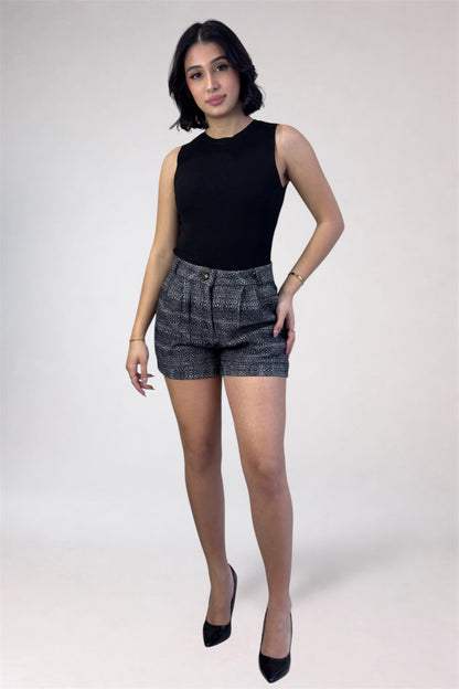 Woman wearing a black sleeveless top and patterned shorts on a white background