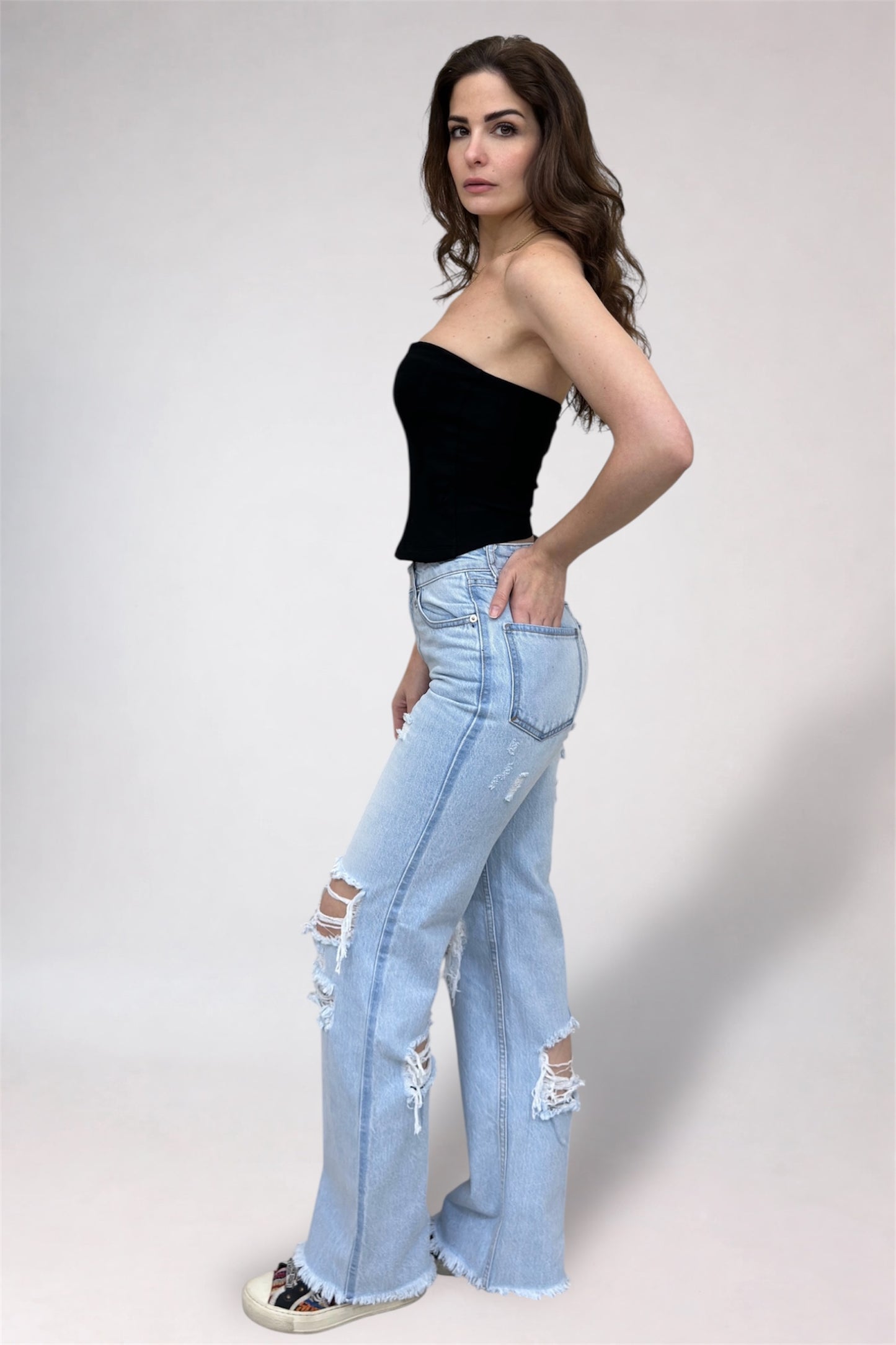 Woman wearing a black top and light blue ripped jeans on a white background