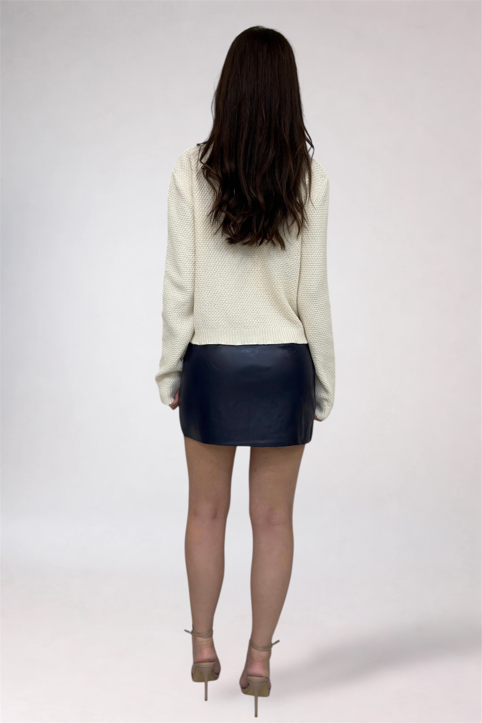 Person wearing a cream sweater and black leather skirt on a white background