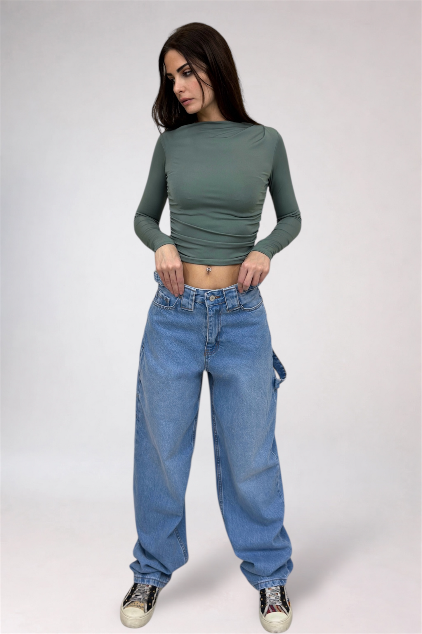Woman wearing a green long-sleeve top and blue jeans on a white background