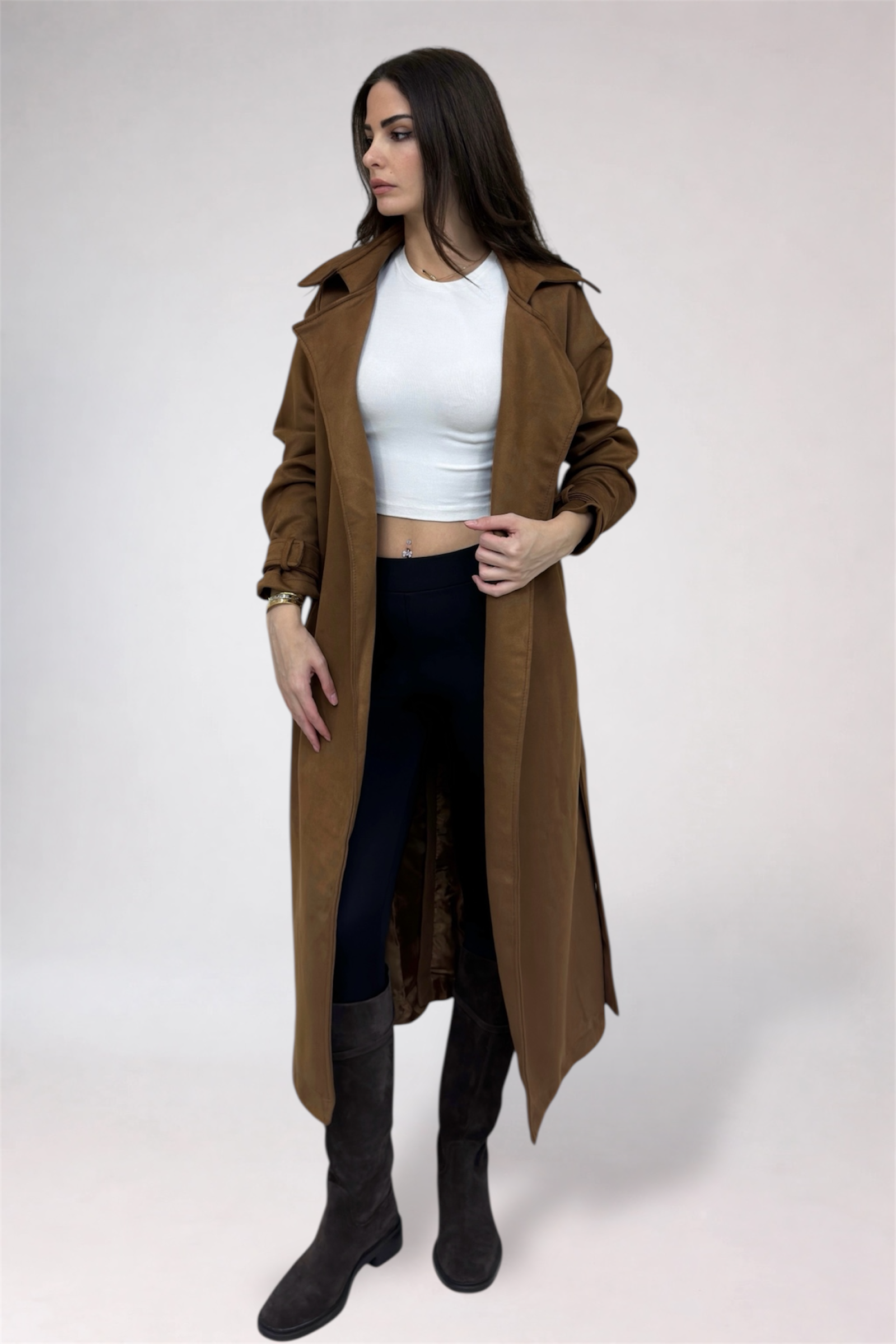 Woman wearing a long brown coat over a white top and black pants on a white background