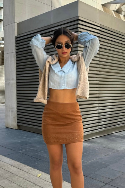 Woman in a stylish outfit with a tan skirt and beige jacket standing in front of a modern building.