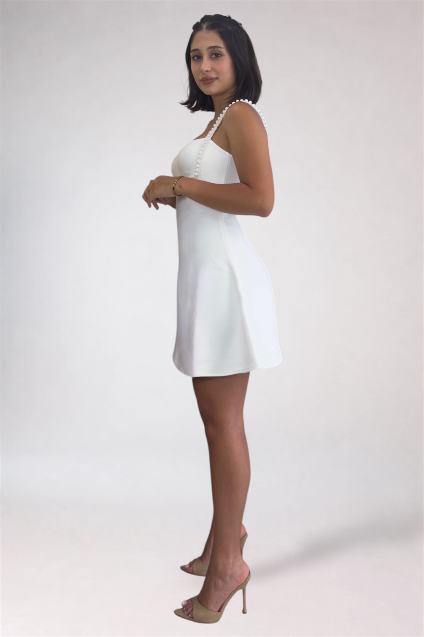 Woman wearing a white dress with a pearl necklace on a plain background