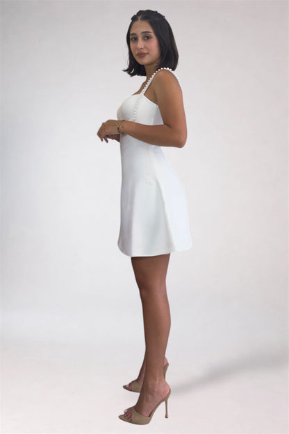 Woman wearing a white dress with a pearl necklace on a plain background