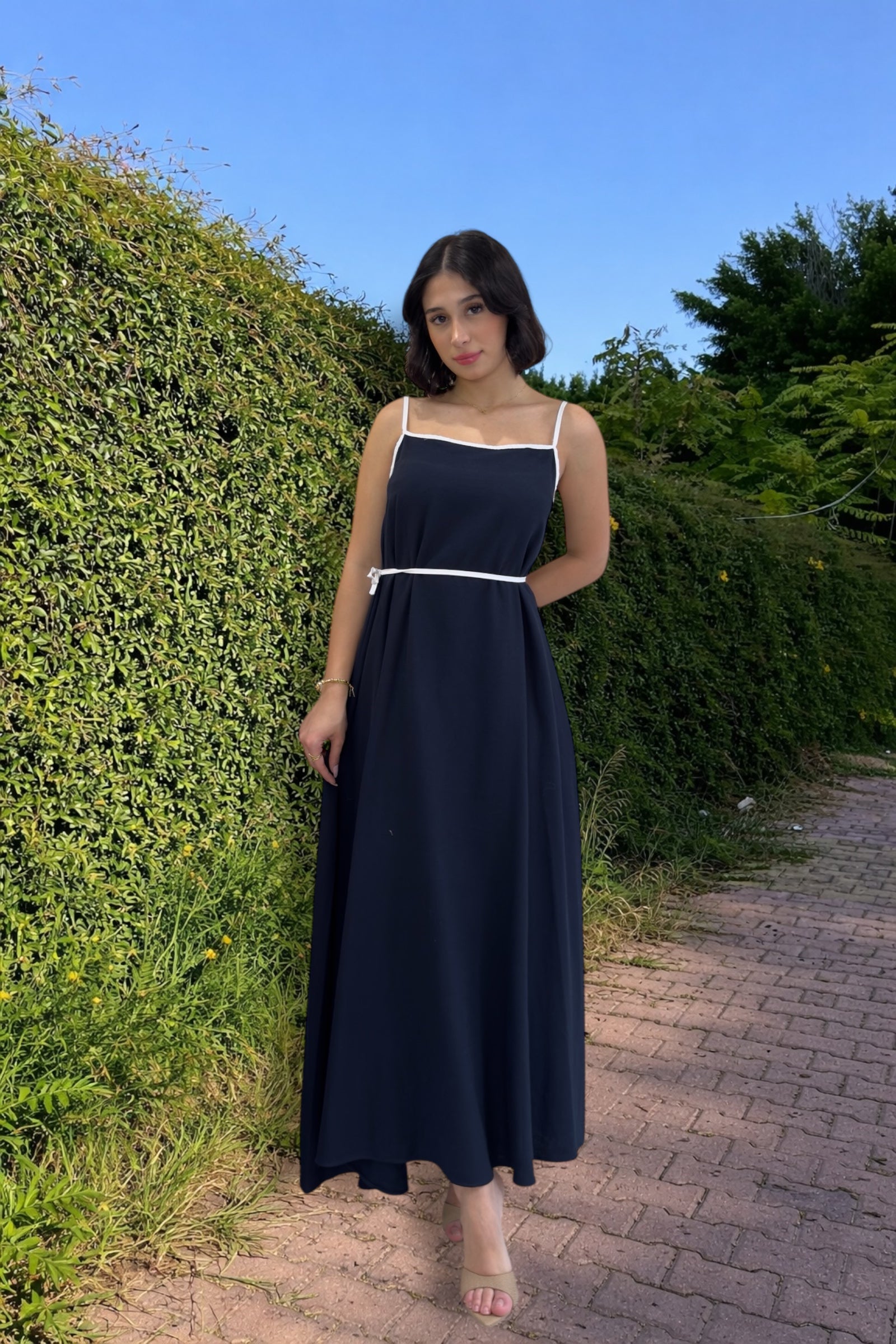 Woman in a navy blue dress standing on a path with greenery around