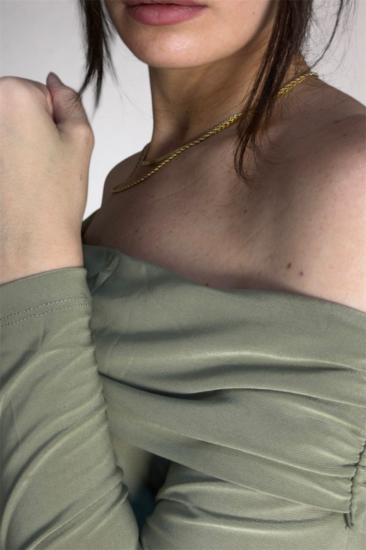 Close-up of a person wearing an off-shoulder green top with a gold necklace.