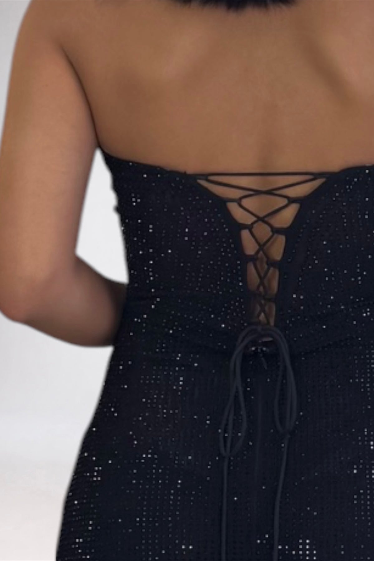 Close-up back view of a woman wearing a strapless black dress with a lace-up back and sequined texture.