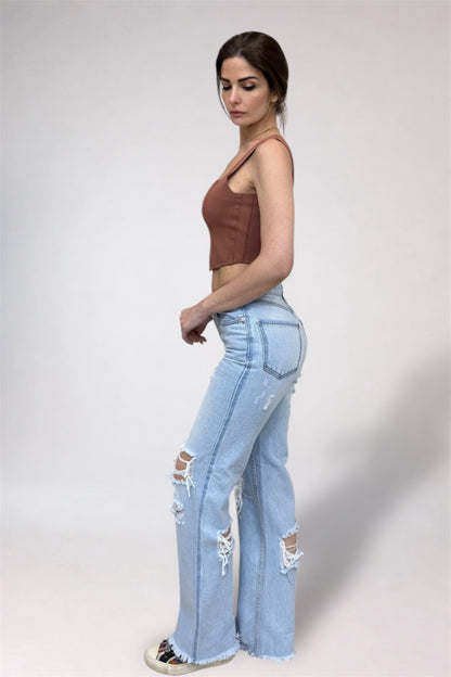 Woman wearing a brown crop top and light blue jeans with rips on a white background