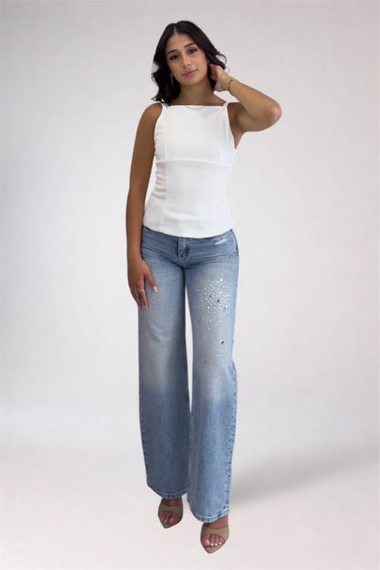 Woman wearing a white top and blue jeans on a plain background