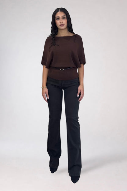 A woman modeling a dark brown short-sleeve top with a wide boat neckline and a thin belt, paired with black flare pants, against a light gray studio background.