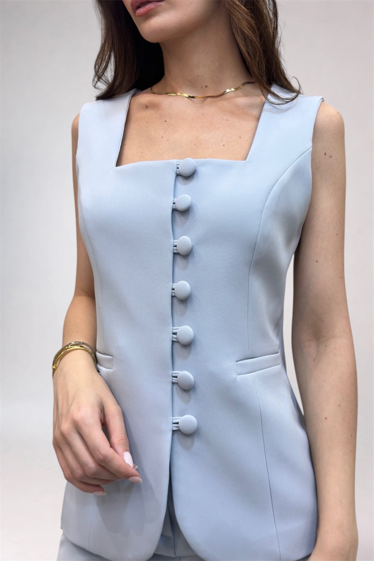 Light blue sleeveless top with button details on a plain background
