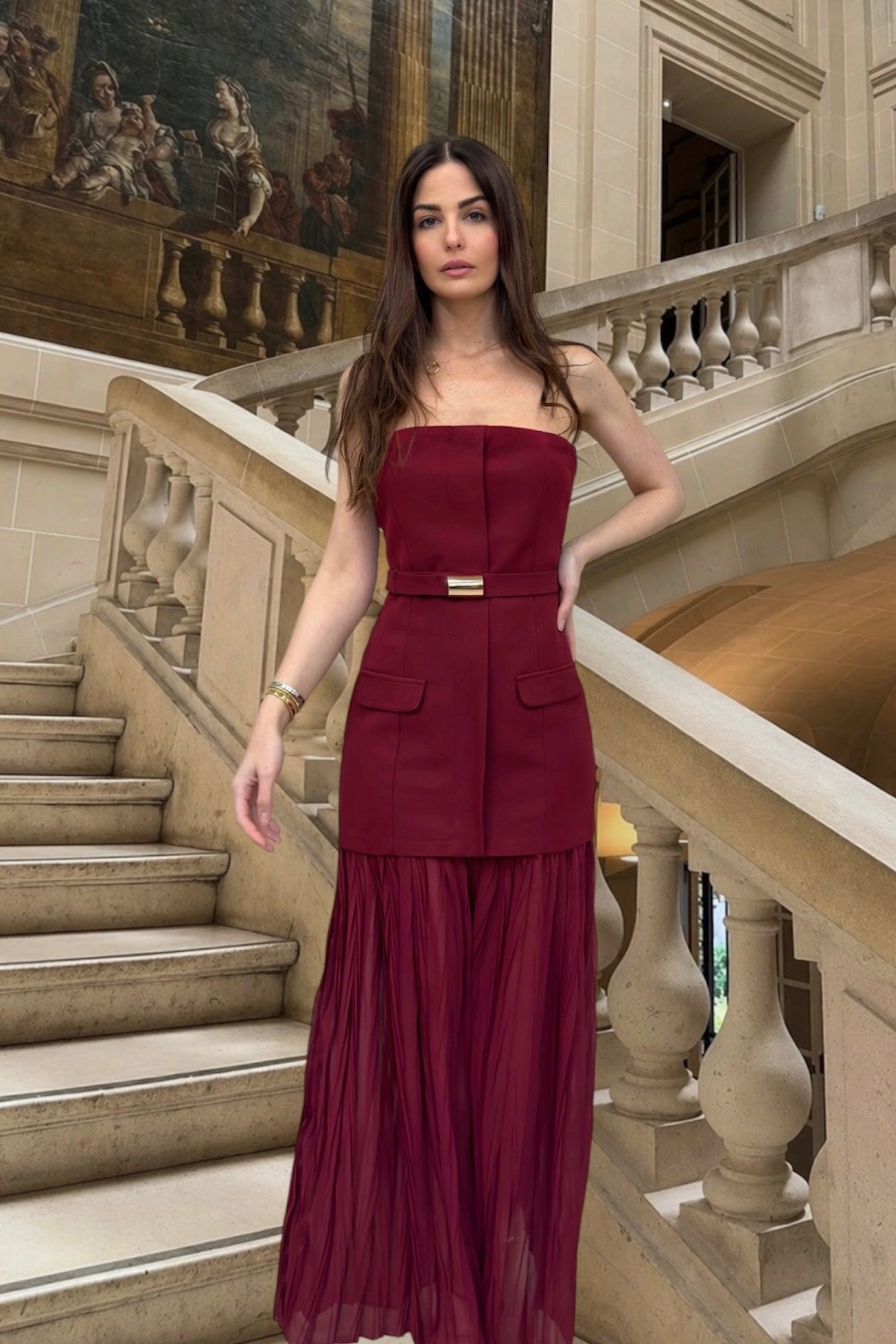 Woman in a burgundy dress standing on a staircase in an elegant interior setting