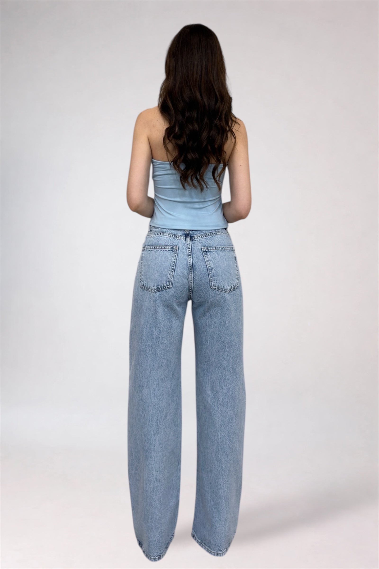 Woman wearing a light blue strapless top and high-waisted jeans on a white background