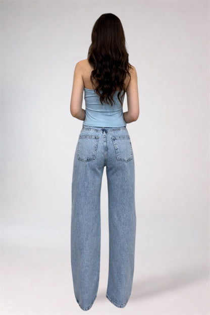Woman wearing a light blue strapless top and high-waisted jeans on a white background