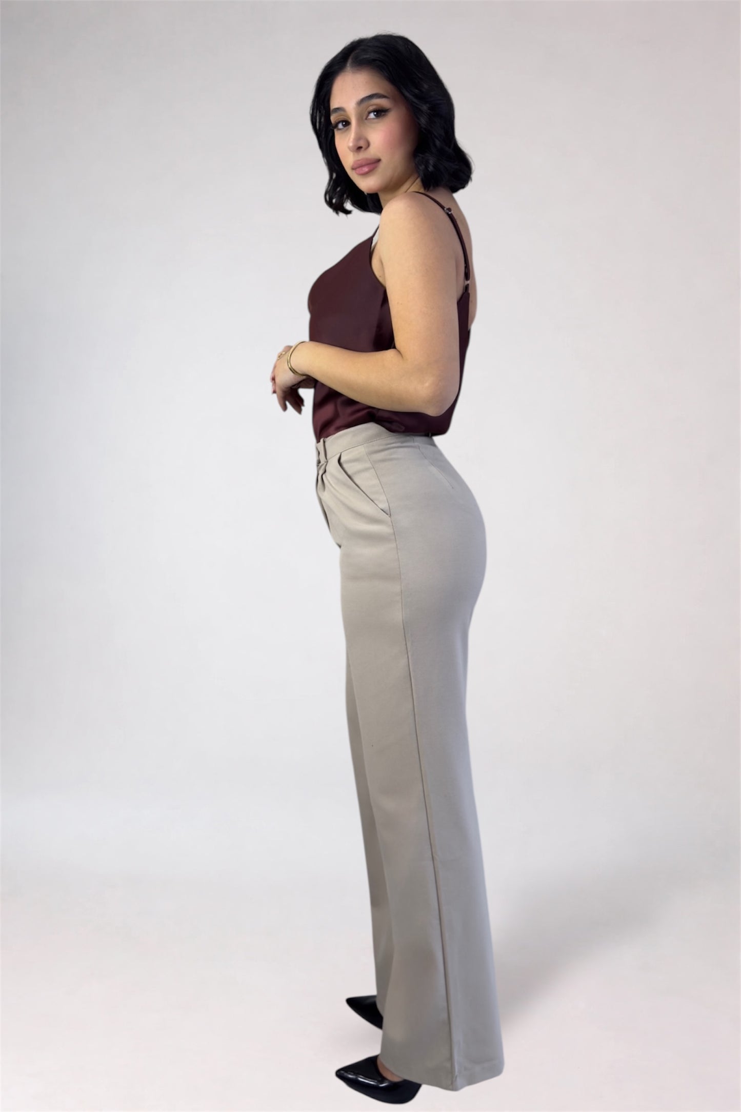 Woman wearing a brown top and light gray pants on a white background