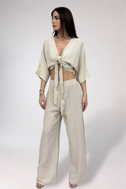 Woman wearing a beige outfit with a tied top and wide-leg pants on a white background