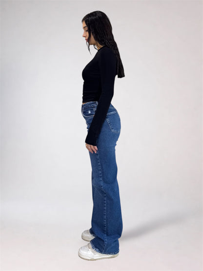 A woman shown in profile wearing a black long-sleeve top, blue flared jeans, and white sneakers against a plain light gray studio background.