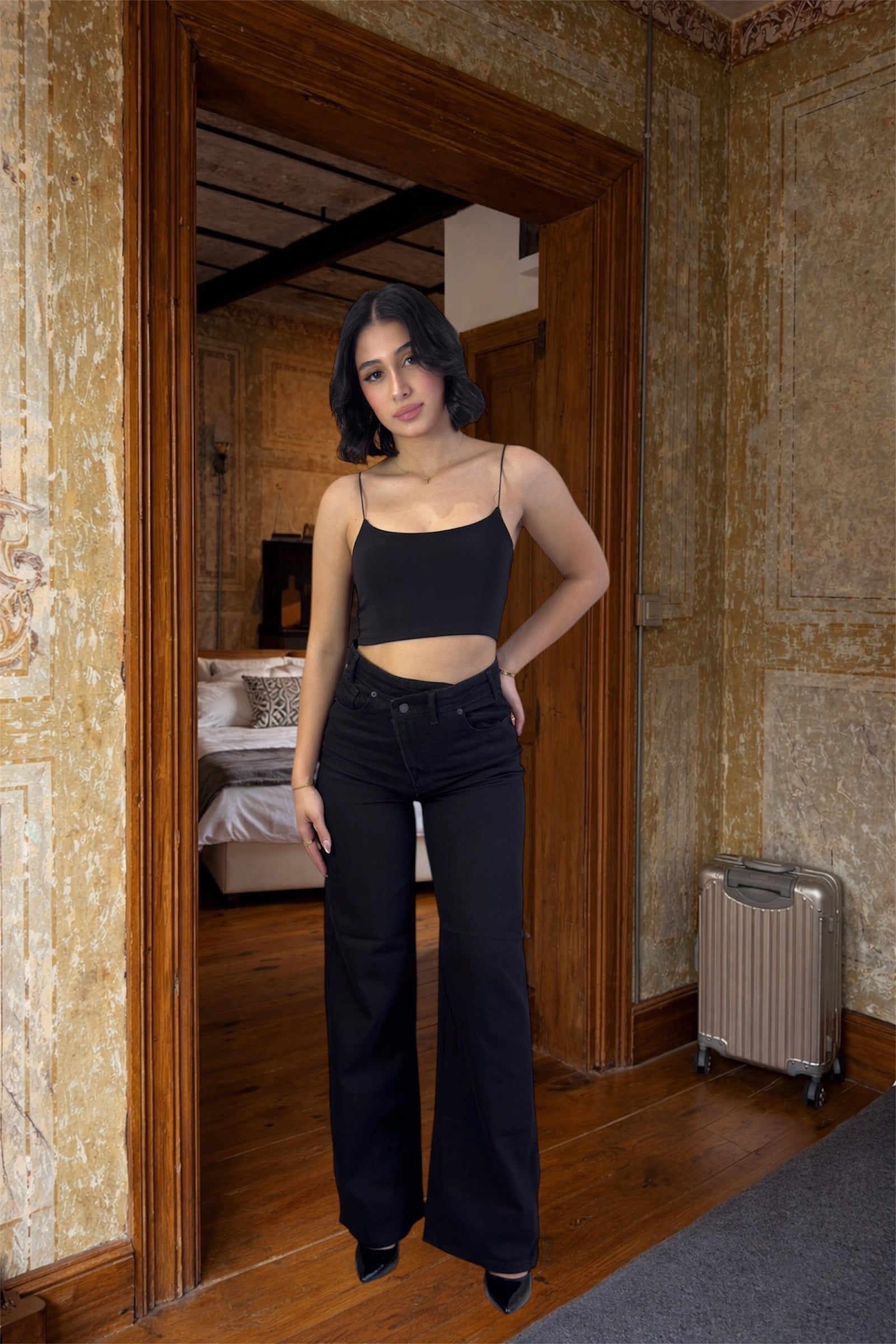 Woman in black top and pants standing in a room with stone walls and wooden floor.