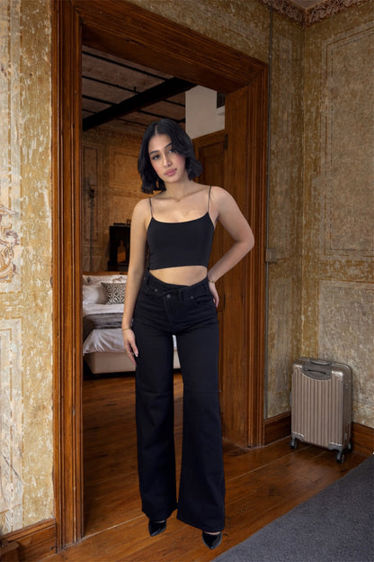 Woman in black top and pants standing in a room with stone walls and wooden floor.