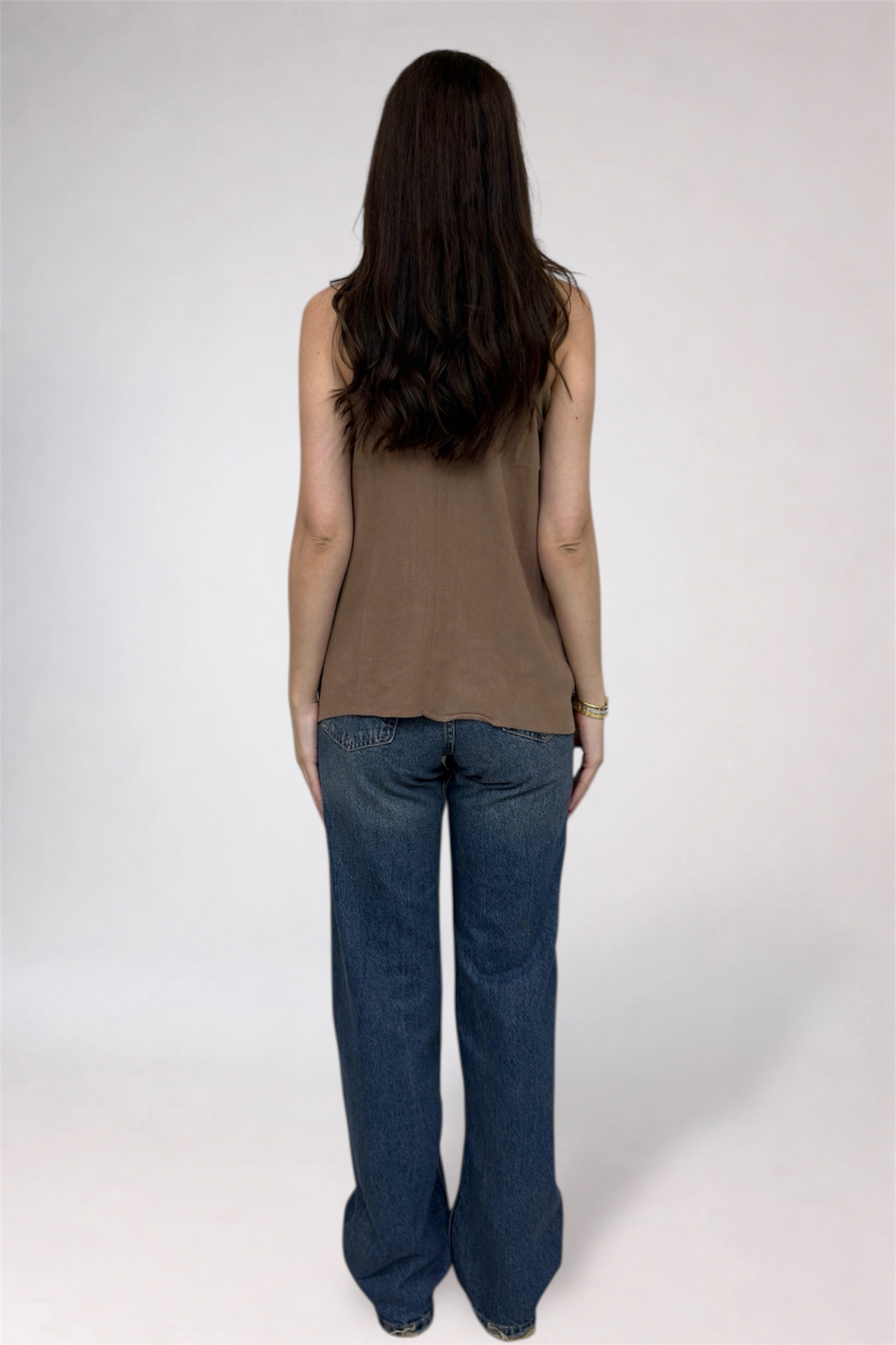 Person wearing a brown sleeveless top and blue jeans on a white background