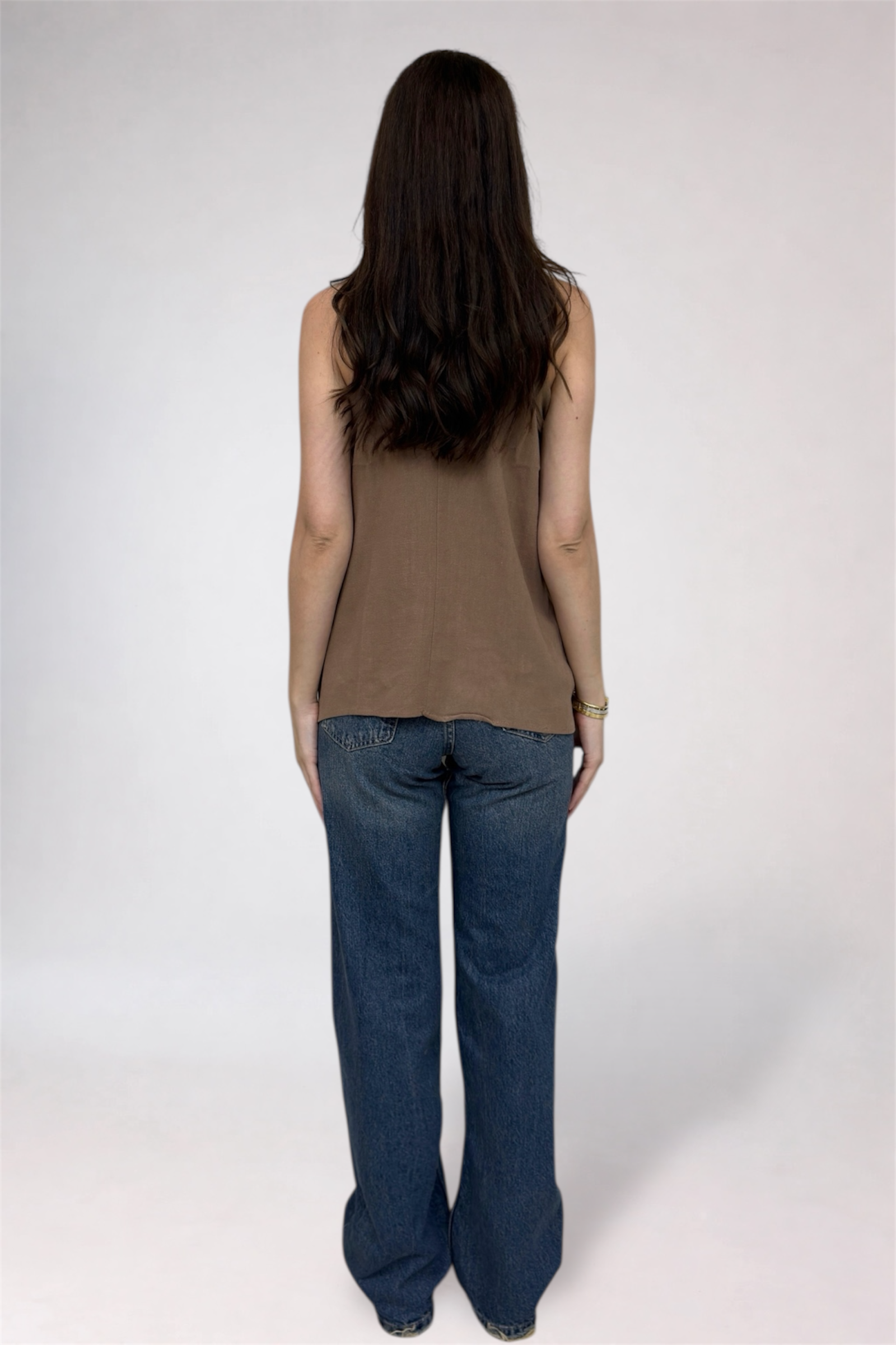 Person wearing a brown sleeveless top and blue jeans on a white background