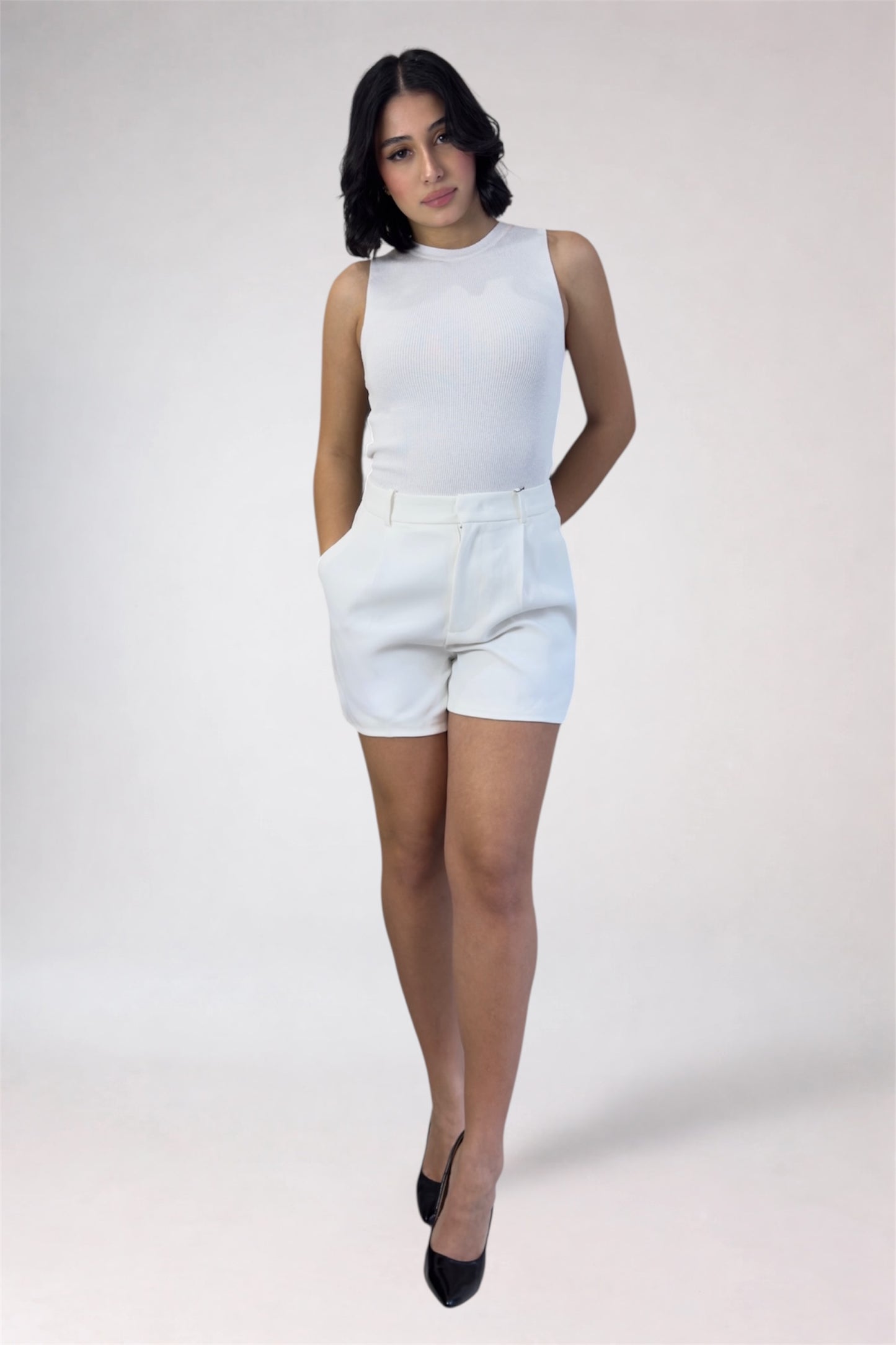 Woman wearing a white sleeveless top and shorts on a plain background