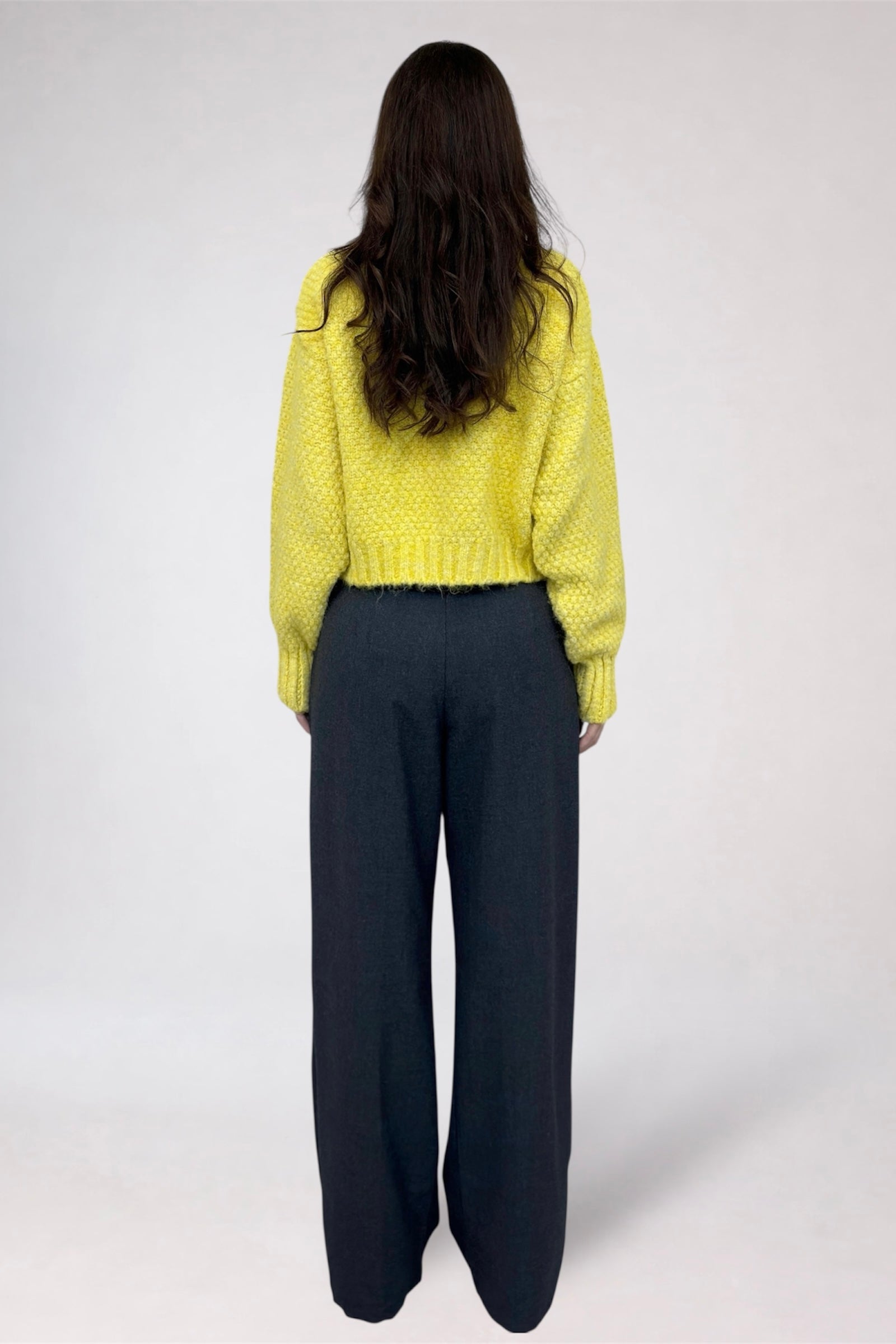 Person wearing a yellow textured sweater and black pants on a white background