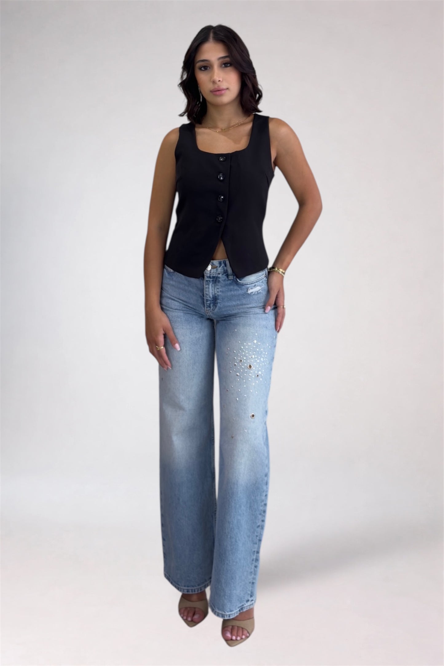 Woman wearing a black sleeveless top and light blue jeans on a white background
