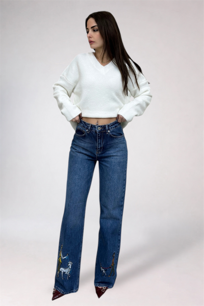 Woman wearing a white sweater and blue jeans with embroidery on a plain background