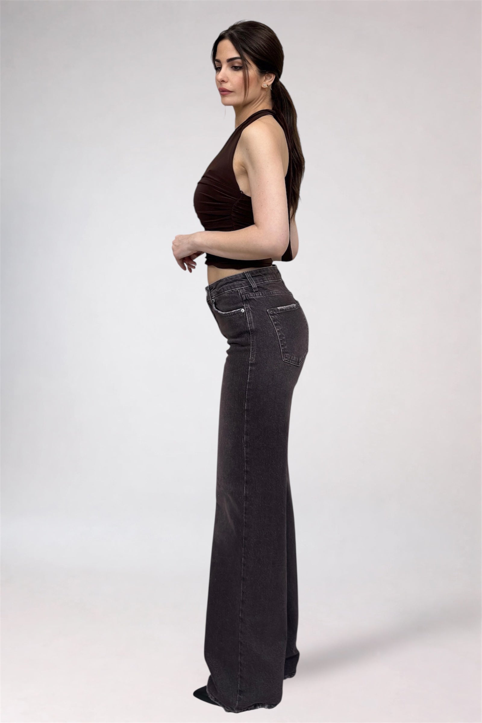 Woman wearing black high-waisted jeans and a brown top on a white background