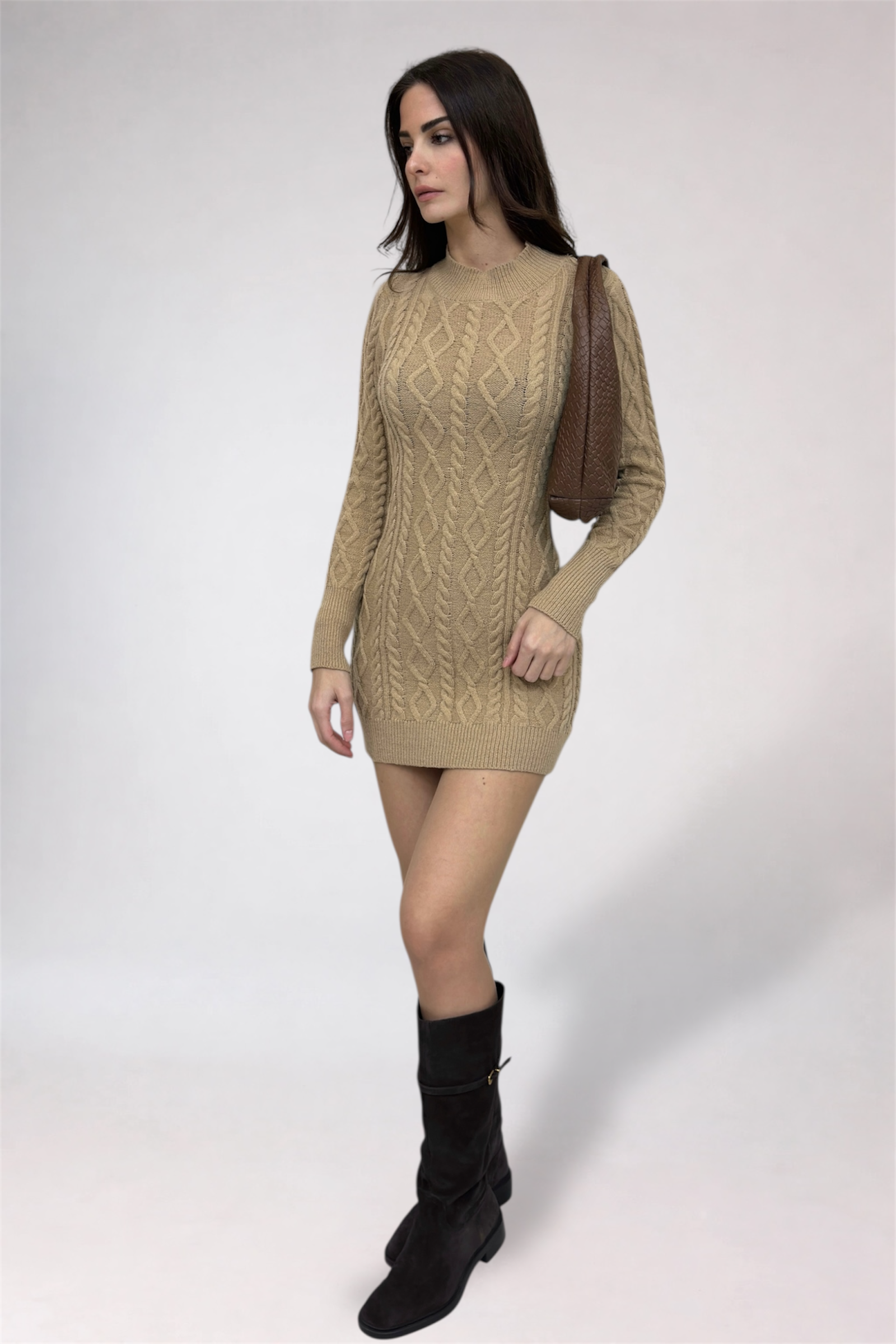 Woman wearing a beige cable knit sweater dress with black boots on a white background